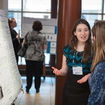 Student presenting their poster to an onlooker, gesturing with her hands